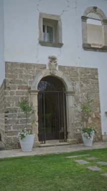 Puglia, İtalya 'daki tarihi taş ev girişinde kırsal kemerli bir kapı, saksı bitkileri ve Avrupa' nın pitoresk bir açık hava ortamında yeşil çimenler yer alıyor..