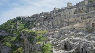 İtalya, Basilicata 'daki tarihi uçurum kenti panoramik manzara. Açık mavi gökyüzü altında antik taş binalar ve yemyeşil alanlar sergileniyor..