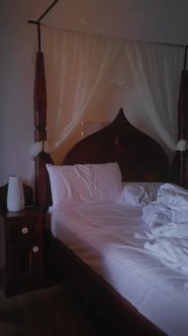 Sönük bir odada beyaz bir yatak, konfor ve sükuneti ön plana çıkarıyor.