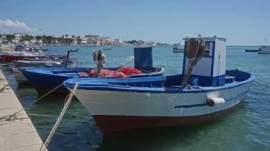 Porto sezeryan, İtalya 'daki bir marinaya yanaşmış balıkçı tekneleri canlı mavi ve beyaz renkleri, güneşli havayı, turkuaz suyu, balıkçılık ekipmanları ve yakındaki sahil binaları vurguluyor..