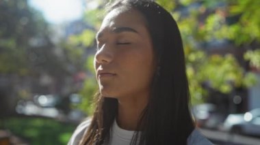 Genç bir kadın, arka planda yeşil ağaçlarla şehir parkında güneşlenmeyi seviyor.