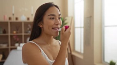 Genç esmer bir kadın huzur ve aydınlık bir atmosferi olan bir sağlık merkezinde dudak kremi sürüyor.