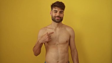 Genç İspanyol adam üstsüz duruyor ve mutlu bir şekilde gülümsüyor sarı bir arka planda.