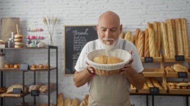 Sakallı olgun bir adam fırında taze ekmek aroması yiyor. Etrafı çeşitli fırınlarla çevrili.