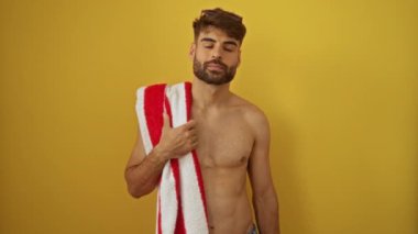 Üzerinde plaj havlusu olan İspanyol gömlekli genç adam izole edilmiş sarı arka planda güvenle gülümsüyor, sağlıklı dişleri olan mutlu ve pozitif.