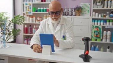 Laboratuvar önlüğü giyen adam eczane tezgahında oturmuş tablet kullanıyor. Etrafı çeşitli sağlık ve güzellik ürünleriyle çevrili..