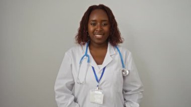 Doktor, genç Afro-Amerikan kadın ayakta, üniforma giyiyor, tamam tabela takıyor, gülümsüyor ve işaret ediyor, dost canlısı ve mükemmel bir şekilde izole edilmiş beyaz arka plan