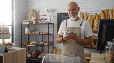 Orta yaşlı, sakallı bir adam pastanede çalışıyor, tezgahın üzerine yeni pişmiş ürünler yerleştiriyor.