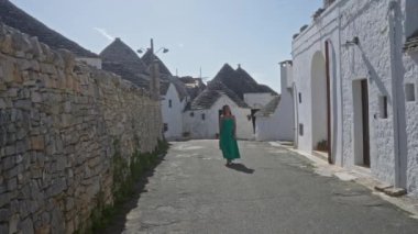 Yeşil elbiseli genç bir İspanyol kadın İtalya 'nın Alberobello şehrinin tarihi sokaklarında yürüyor. Arka planda benzersiz Trulli evleri var. Çekici bir Avrupa manzarası yaratıyor..