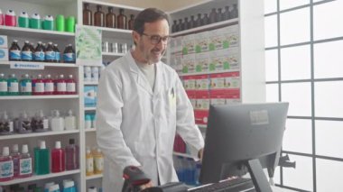 Eczanede laboratuvar önlüğü ve gözlüğü takan, video görüşmesi sırasında bilgisayarda çalışan olgun bir İspanyol..