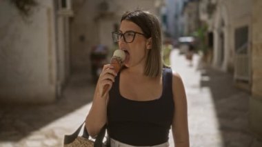 Yaşlı Puglia kasabasının sokaklarında dondurma yiyen genç bir kadın, Avrupa 'da bir yaz gününün tadını çıkarıyor..
