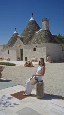 Genç İspanyol kadın alberobello, İtalya 'da, açık havada oturuyor, geleneksel Trulli evlerinin önünde parlak mavi bir gökyüzünün altında, beyaz elbiseler giyiyor ve elinde bir hasır çanta tutuyor..