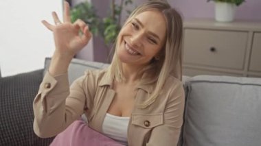 Kanepede oturan genç sarışın kadın olumlu gülümsüyor ve el ve parmaklarıyla 