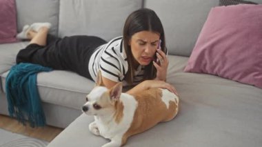 Genç bir İspanyol kadın oturma odasındaki kanepede Chihuahua köpeğiyle birlikte rahat bir apartman dairesinde akıllı telefonuyla iletişim kuruyor..