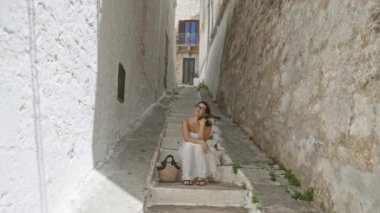 Taş basamaklarda elinde sepetle oturan genç, güzel İspanyol kadın. Eski bir şehir olan Ostuni 'de, Puglia' da, İtalya 'da, Avrupai' de. Etrafı boyalı binalarla çevrili..