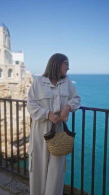 Genç ve güzel bir İspanyol kadın polignano 'da bir bakış açısında duruyor. Bir kısrak, puglia, İtalya, manzaranın tadını çıkarırken kırsal dokuma çantasını tutuyor..