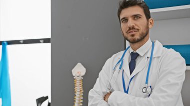 Handsome hispanic man in a white lab coat posing confidently in a medical clinic. clipart