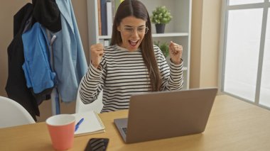 Heyecanlı İspanyol kadın ev ofisinin dizüstü bilgisayarında başarıyı kutluyor.