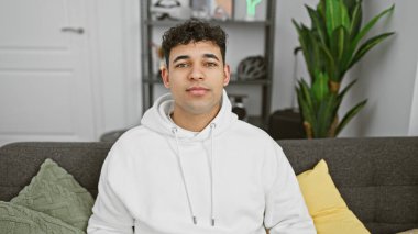 Kapalı bir koltukta oturan yakışıklı bir gencin portresi. Arka planda saksı bitkisi var..