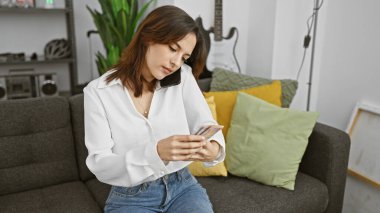 Genç İspanyol kadın evde Kolombiya pezosu sayıyor, gri bir kanepede oturuyor..