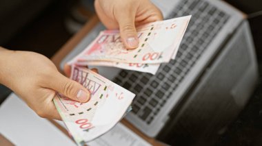 Genç Asyalı Hong Kong dolarlarını arka planda dizüstü bilgisayarla sayıyor..