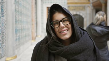 Gözlüklü, şallı, gülümseyen genç bir İspanyol kadın İstanbul 'da bir şiltede duruyor..