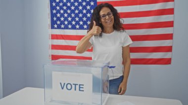 Kapalı bir seçim merkezinde arka planda Amerikan bayrağı olan bir kadın oy veriyor.