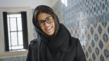 Türkçe fayansların önünde durup İstanbul 'un zengin kültürel mirasını anımsatan, gözlüklü, başörtüsü takan genç bir kadın..