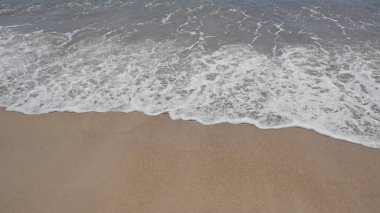 Sakin bir sahil sahnesi Yumuşak dalgalar ve kumlu bir sahil berrak bir gökyüzü altında