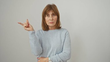 Kısa saçlı olgun bir kadın, beyaz izole edilmiş bir arkaplanı işaret ediyor. Yön ve belirleyici bir jest yapıyor..