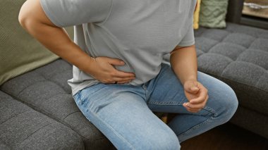 Gri bir kanepede otururken midesi ağrıyan genç bir Asyalı..