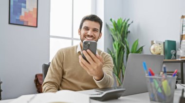 Neşeli İspanyol bir adam modern bir ofiste selfie çekiyor, profesyonellik ve memnuniyet yayıyor..