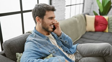 Modern oturma odasında telefonla konuşurken gülümseyen İspanyol adam.