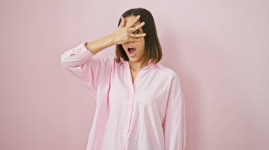 Şaşırmış genç bir kadın, pembe izole edilmiş arka planda elleri ile yüzünü kapatıyor..