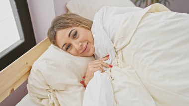 Kafkasyalı sakin bir kadın rahat bir yatak odasında huzur ve konforun somutlaştırıldığı rahat bir anın tadını çıkarıyor..