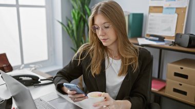 Profesyonel, genç, beyaz bir kadın modern bir ofis ortamında akıllı telefon kullanıyor..