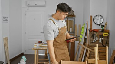 Marangozluk atölyesinde genç bir Asyalı adam, kapalı bir tabletteki planları inceliyor..