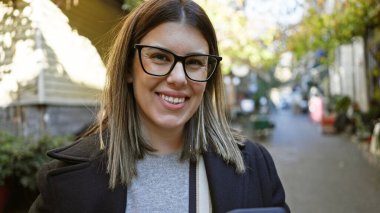 Gözlüklü, gülümseyen esmer kadın tarihi İstanbul caddesinde poz veriyor, gençliği ve şehir turizmini somutlaştırıyor..
