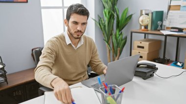 Modern ofis içinde dizüstü bilgisayarda çalışan yakışıklı İspanyol.