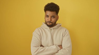 Kendine güvenen Afro-Amerikan bir adam. Sıradan giyinmiş. Sarı arka planda kollarını kavuşturmuş poz veriyor.