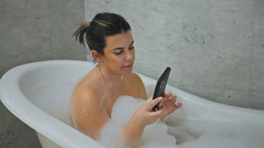 Genç bir İspanyol kadın telefonuna bakarken köpük banyosunda dinleniyor..