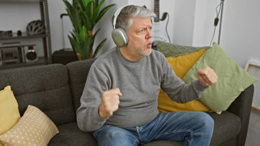 Olgun bir adam, modern oturma odasında heyecanla şarkı söyleyerek kulaklıkla müzik dinlemekten hoşlanır..