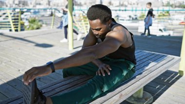 Genç bir Afro-Amerikan sporcusu şehrin ahşap iskelesinde güneşli bir şehir zeminiyle geriniyor..