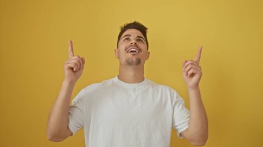 Yakışıklı genç adam yukarıya bakıyor, sarı arka planda izole edilmiş, pozitifliğini ifade ediyor..