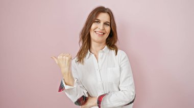 Gülümseyen orta yaşlı bir kadın pembe izole bir arka plana başparmak işareti yapıyor, pozitiflik ve kendine güveni gösteriyor..