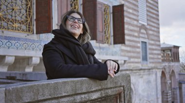 Gülümseyen kadın, gözlüklü, taş parmaklıklara yaslanmış, Topkapı Sarayı 'nda, İstanbul' da, seyahat ve kültür sergiliyor..