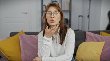 Kafkasyalı genç bir kadın rahat ve rahat bir pozda renkli yastıklarla evinde oturuyor..