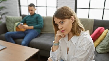 A thoughtful woman and distracted man sharing a couch, portraying relationship issues in a modern living room. clipart