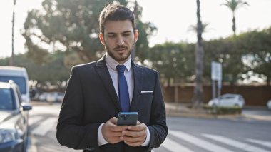 Yakışıklı İspanyol takım elbiseli iş adamı güneşli bir şehirde akıllı telefon kullanıyor.