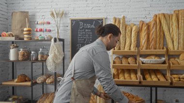 İçerideki fırında bıyıklı İspanyol bir adam arka planda hamur işleri ve karatahta menüleriyle ahşap raflarda taze ekmek düzenliyor.